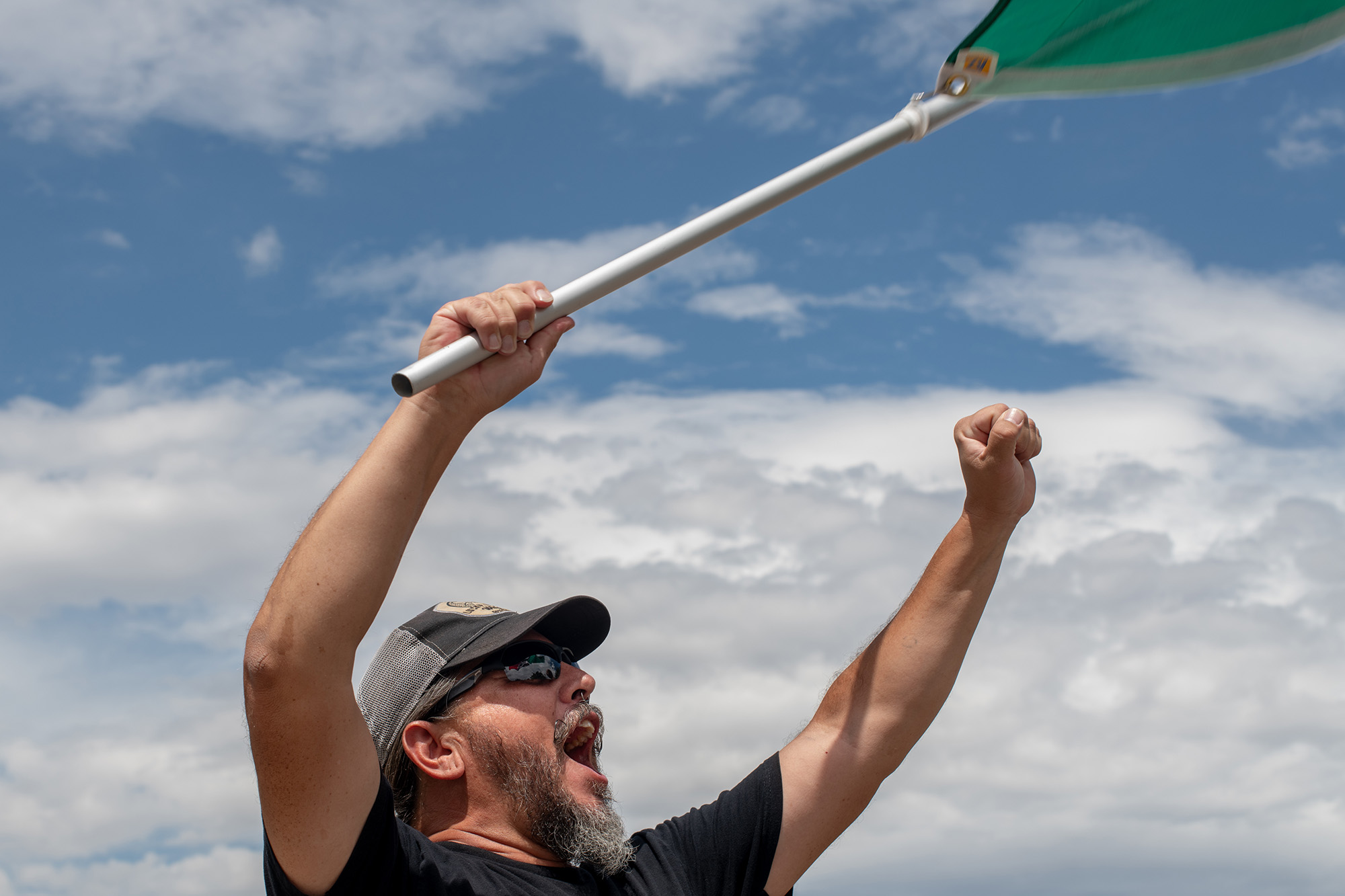 Jason Valdez, shouting, holds his hands in the air. A flag waves in his right hand as he forms a fist with his left.