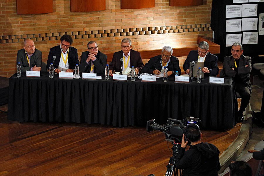In Colombia, seven former members of the FARC were convicted in 2025 for war crimes and crimes against humanity. Photo: Seven people (including one person who is not among the seven convicted) are seated at a long table, with their names written in front of them.