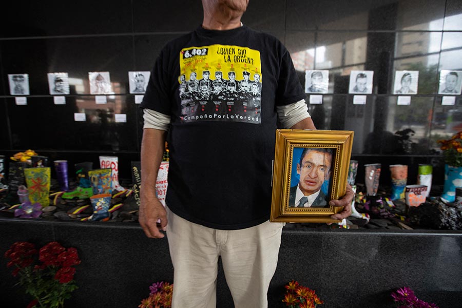 In Colombia, a relative of a victim of an extrajudicial execution known as a ‘false positive’ holds a portrait and wears a T-shirt denouncing this Colombian scandal. In the background, other portraits and boots are displayed in their memory.