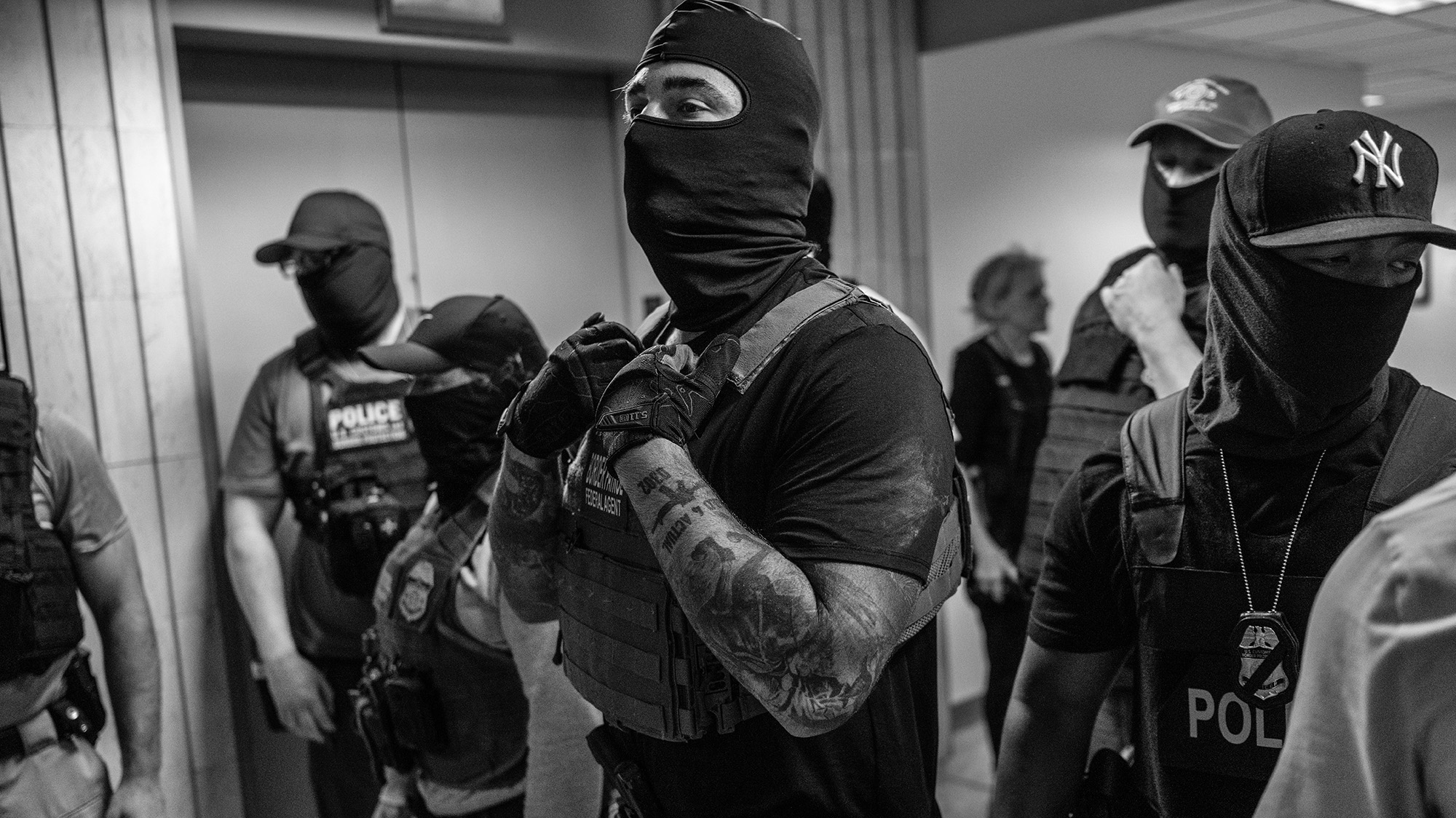 Group of masked ICE agents standing in hallway.