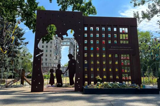 Monuments commemorating war crimes in Ukraine. Photo: A monument dedicated to the victims of war crimes depicts a missing family seen through a hole in a wall. In the background is a destroyed multi-storey building.